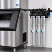 Pentair Everpure water filter system with three silver cylindrical filter cartridges mounted on a black wall-mounted bracket next to a stainless steel ice machine.